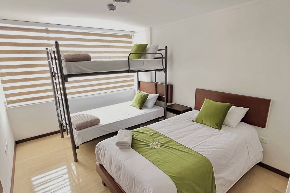 A hotel room with a bunk bed, a single bed, and a wooden floor.