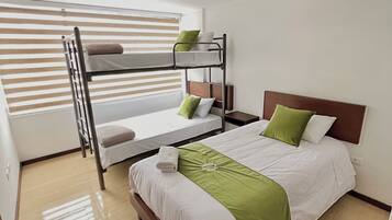 A hotel room with a bunk bed, a single bed, and a wooden floor.