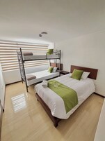 A hotel room with a bunk bed, a single bed, and a wooden floor.