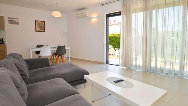 A modern living room with a grey sectional sofa, a white coffee table, and a dining area with a small table and chairs. - Family Friendly Spacious Apartment With Garden and Terrace (Rovinj)