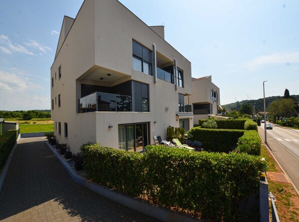 A modern two-story residential building with large windows, a balcony, and a well-maintained garden.