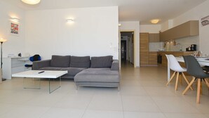 A modern living room with a grey sectional sofa, a white coffee table, and a dining area with a wooden table and chairs. - Family Friendly Spacious Apartment With Garden and Terrace (Rovinj)