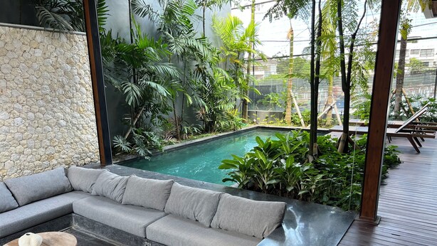 A modern outdoor seating area with a pool, stone wall, and lush greenery.