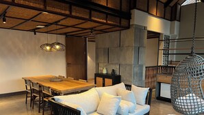 A modern living room with a wooden dining table, a sofa with cushions, a hanging chair, and a stone wall.