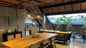 A spacious dining area with a long wooden table and chairs, a black cabinet with woven shelves, and a hanging light fixture.
