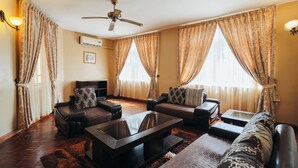 A living room with a ceiling fan, two sofas, a coffee table, and a TV. - Amariah Apartments TPDC Mikocheni (Dar es Salaam)