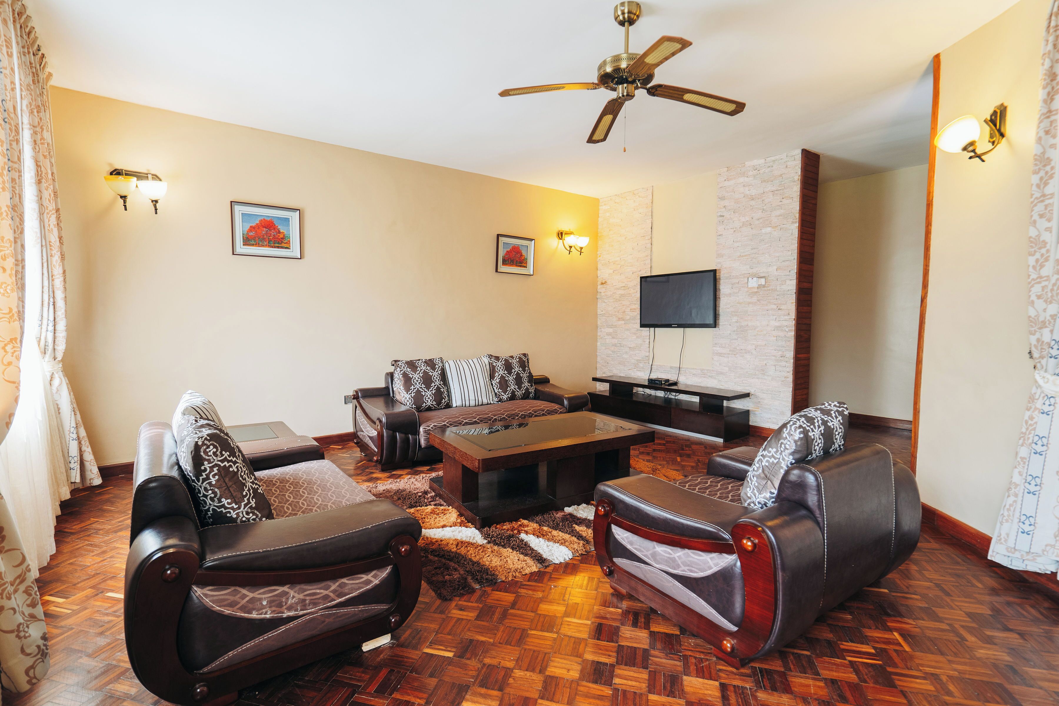 A living room with a sofa set, a coffee table, a flat-screen TV, and a ceiling fan.
