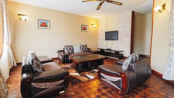 A living room with a sofa set, a coffee table, a flat-screen TV, and a ceiling fan.