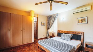 A bedroom with a wooden bed, a ceiling fan, a wardrobe, and a window with curtains. - Amariah Apartments TPDC Mikocheni (Dar es Salaam)