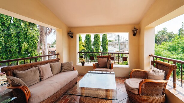 A balcony with a wicker sofa, a glass coffee table, and wicker chairs. - Amariah Apartments TPDC Mikocheni (Dar es Salaam)