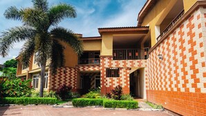A two-story house with a tiled exterior, a balcony, and a well-maintained garden with a palm tree. - Amariah Apartments TPDC Mikocheni (Dar es Salaam)