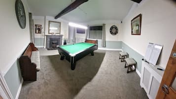 A pool room with a pool table, a dartboard, a fireplace, and a mirror.
