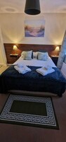 Una cama bien tendida con una colcha azul oscuro y almohadas blancas, un tapiz decorativo y una alfombra con estampado geométrico.