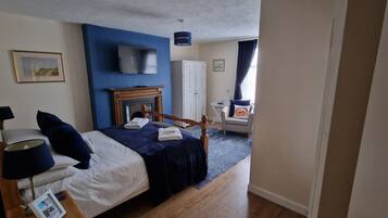 A bedroom with a bed, a TV mounted above it, a fireplace, and a window with curtains.