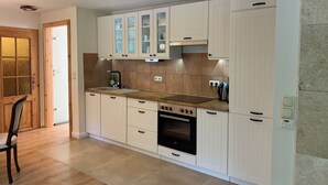 A modern kitchen with white cabinetry, a built-in oven, and a countertop with a kettle. - Pension Gesundbrunnen (Mueglitztal)