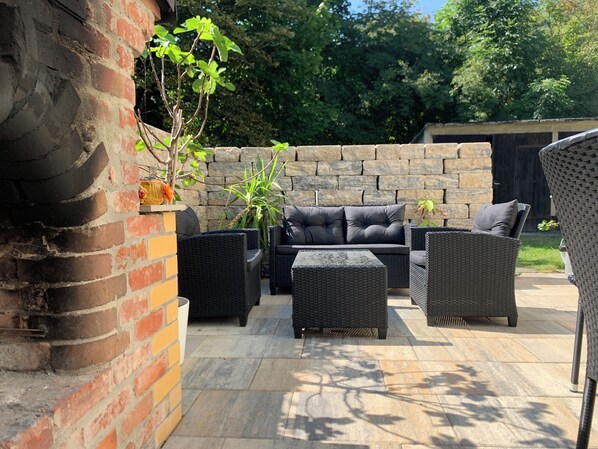 An outdoor patio area with wicker furniture, a brick wall, and a stone floor. - Pension Gesundbrunnen (Mueglitztal)