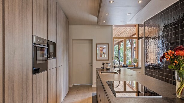 A modern kitchen with wooden cabinets, a built-in oven, and a large island with a sink.