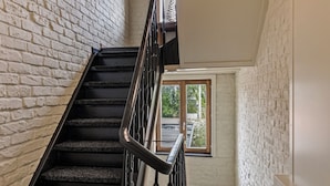 A staircase with a wooden finish, white brick walls, and a window at the top.