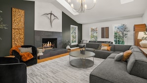 Un salon moderne doté d’une cheminée, de canapés modulaires, d’une table basse ronde et d’une grande fenêtre laissant entrer la lumière naturelle.