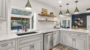 Une cuisine moderne avec des meubles blancs, un lave-vaisselle encastré et des luminaires suspendus.