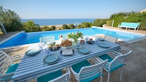 A dining table set with plates, glasses, and a centerpiece, overlooking a pool and the sea.