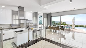 A modern kitchen with a central island, stainless steel appliances, and a dining area with a view of the sea.