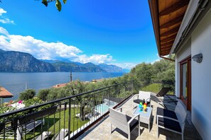 Un balcón con mobiliario exterior, una piscina y una vista panorámica de montañas y un lago.