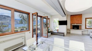 A modern living room with large windows, a fireplace, and a glass dining table. - MAISON SABINA WITH WONDERFUL LAKE VIEW, HYDROMASSAGE AND PRIVATE GARDEN (BRENZONE SUL GARDA)