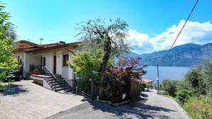 A two-story house with a red door, a staircase, and a view of a lake and mountains. - MAISON SABINA WITH WONDERFUL LAKE VIEW, HYDROMASSAGE AND PRIVATE GARDEN (BRENZONE SUL GARDA)