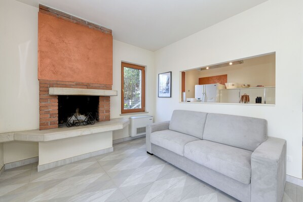 Una sala de estar con chimenea, un sofá y una cocina con armarios y un refrigerador.