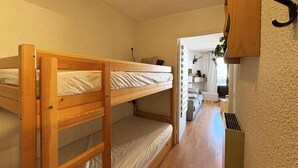 A bunk bed room with a wooden headboard, a bedside table, and a small shelf. There is a door leading to a bathroom with a mirror and a sink. - 10m from ski slopes, 4th floor, view ski slopes, balcony, tv, 22m², Les Orres (Les Orres)
