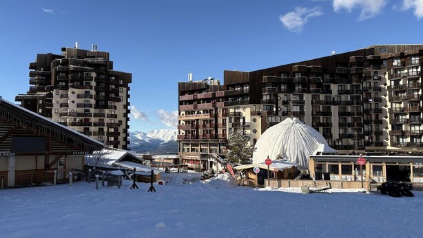 A snow-covered outdoor area with modern buildings, a ski lift, and a mountain backdrop. - 10m from ski slopes, 4th floor, view ski slopes, balcony, tv, 22m², Les Orres (Les Orres)