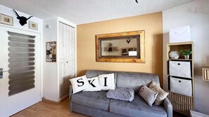 A cozy living room with a grey sofa, a mirror on the wall, and a door with horizontal blinds.