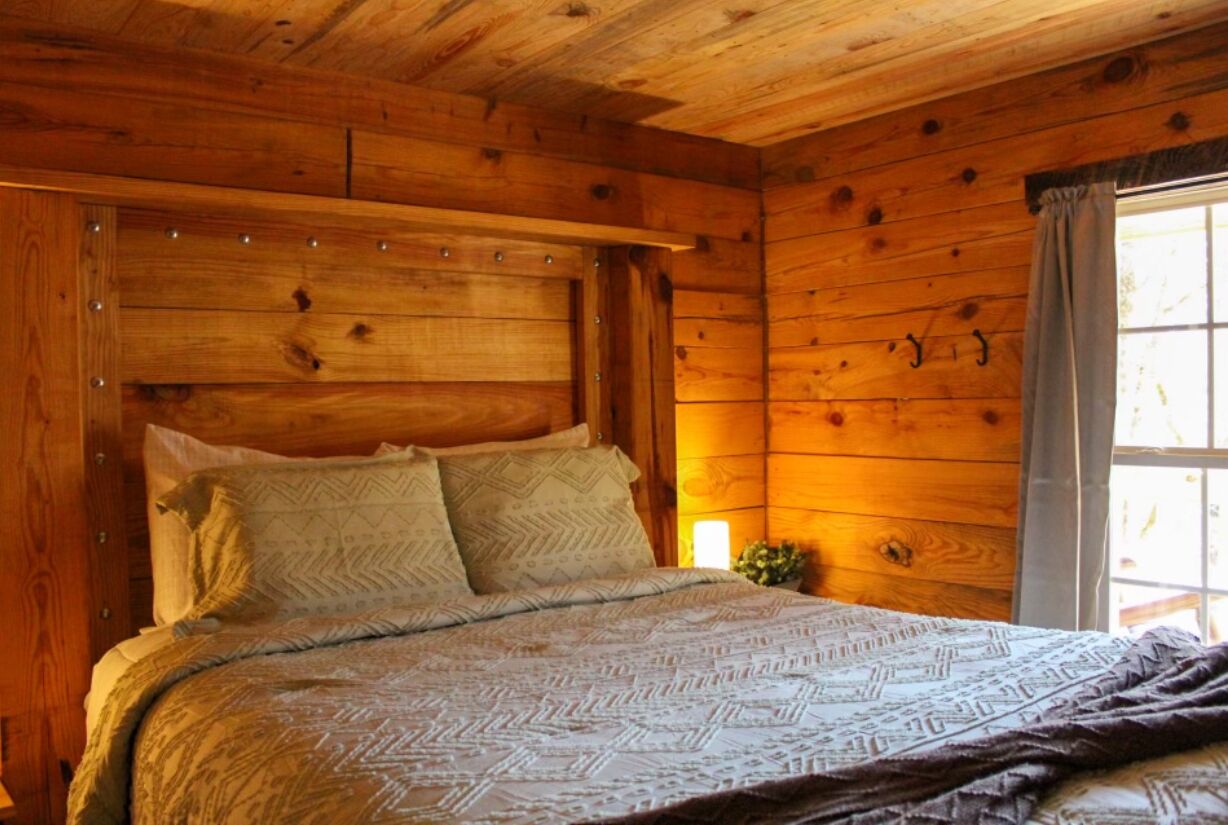 A wooden cabin bedroom with a bed, pillows, and a nightstand.