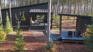 A modern cabin with a deck, outdoor seating, and a forest backdrop. - Brand New Black Fox Cabin (Sprucedale)