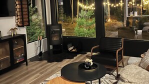 A modern living room with a large window, a fireplace, and a cozy seating area. - Brand New Black Fox Cabin (Sprucedale)