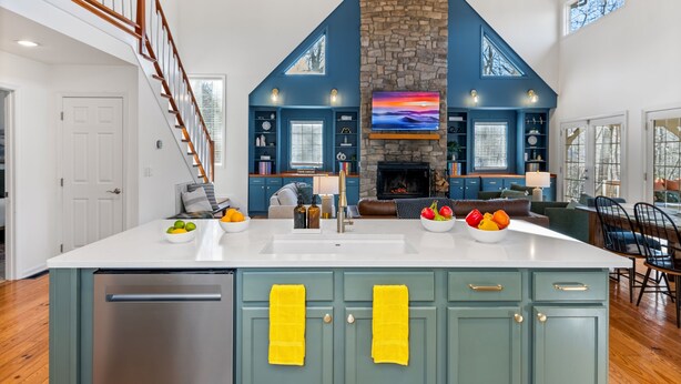 A spacious kitchen with a central island, a stone fireplace, and a dining area with a high ceiling and wooden beams.