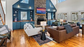 A spacious living room with a stone fireplace, blue accent walls, and a wooden staircase.