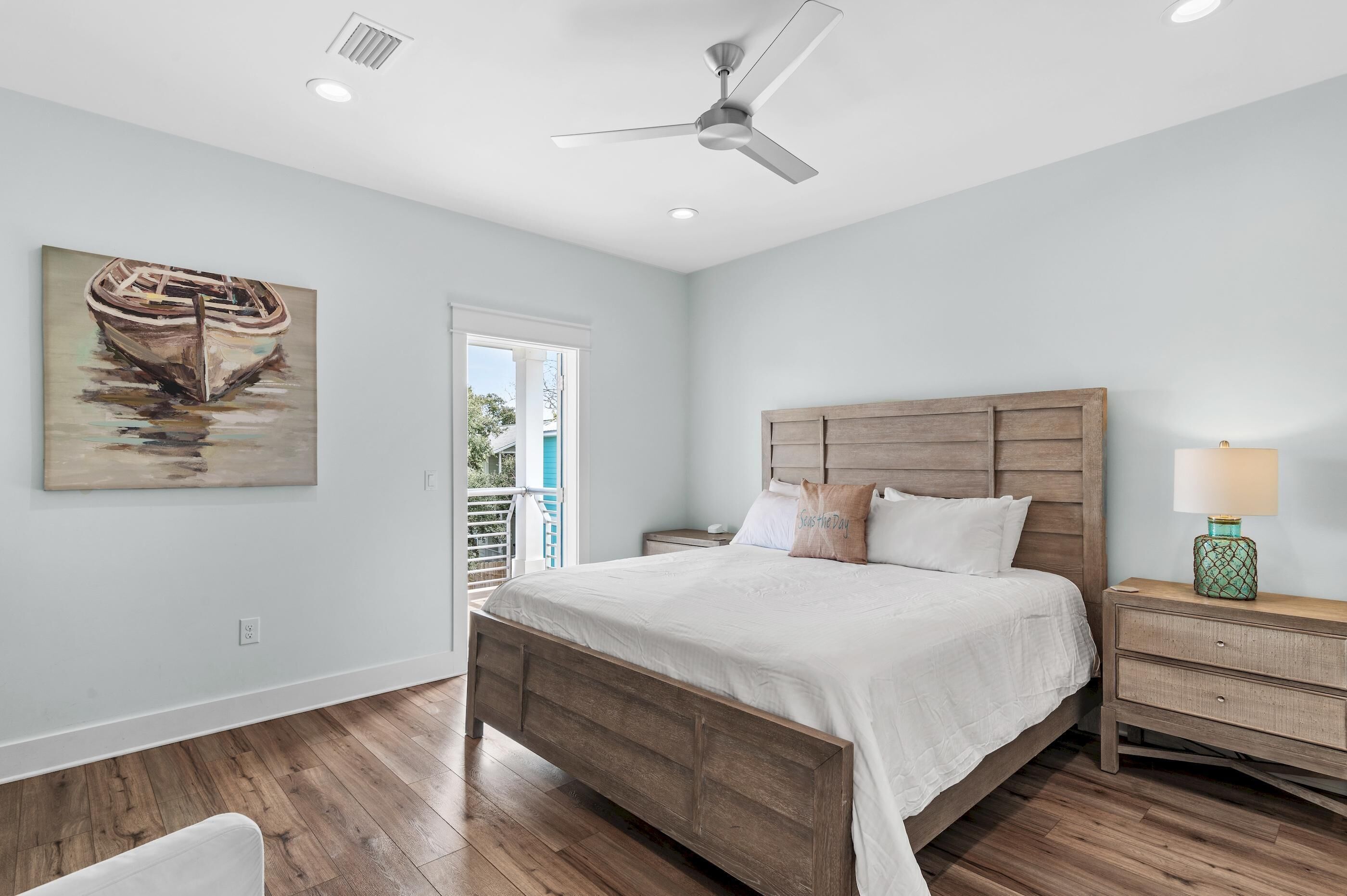 Une chambre à coucher avec un lit en bois, une table de chevet avec une lampe, un ventilateur de plafond et un tableau représentant un bateau accroché au mur.