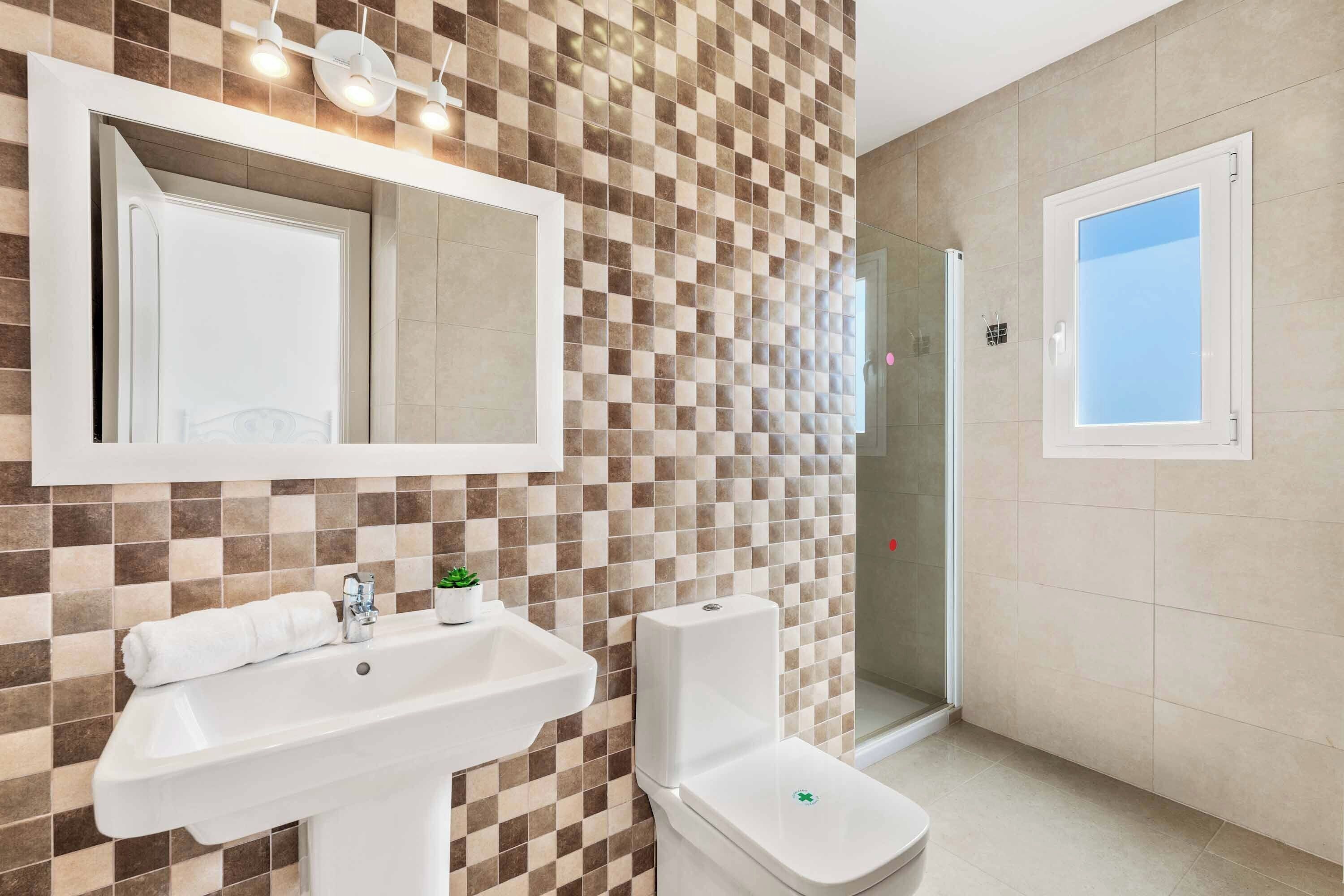 Un baño con pared de baldosas a cuadros, un lavamanos blanco, un inodoro y una cabina de ducha de cristal.