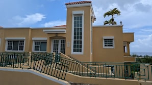 A building with a beige facade, a red-tiled roof, and a central tower with a large window. - Ocean View Rooftop Villa Near El Yunque Sleeps 6 (Rio Grande)
