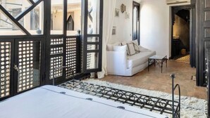 A room with a large window, a white sofa, a small table, and a bed with a white headboard. - Riad basidi (Marrakech)