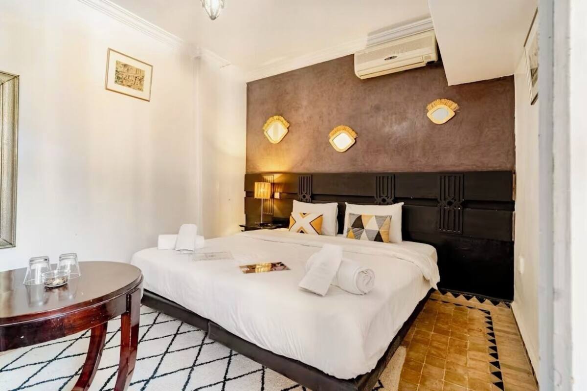A hotel room with a large bed, a round wooden table, and a patterned floor.