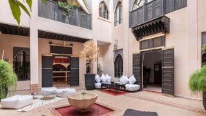A courtyard with outdoor seating, a decorative fountain, and a building with traditional Moroccan architecture. - Riad basidi (Marrakech)