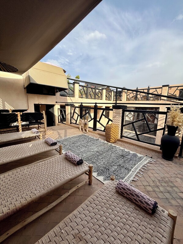 A rooftop terrace with woven lounge chairs, a large woven rug, and a potted plant.