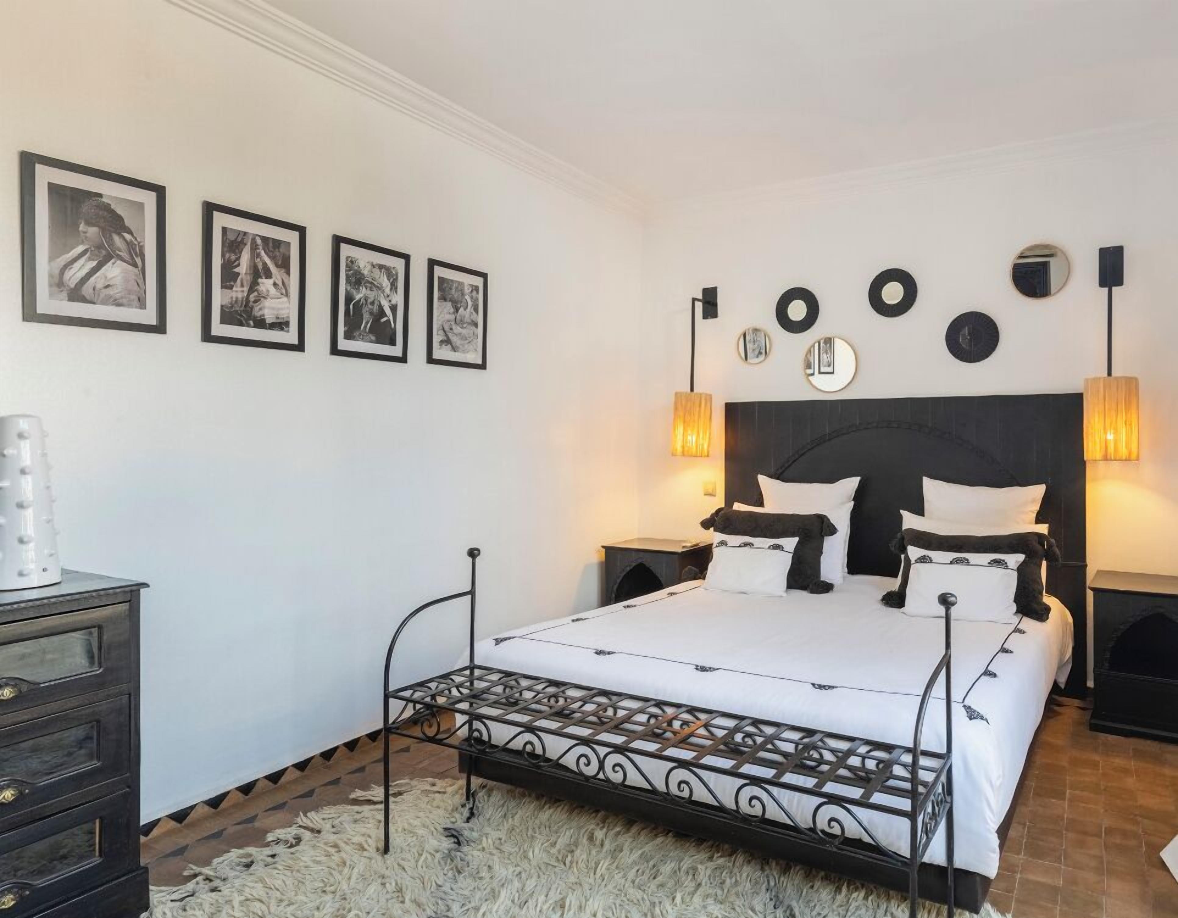 Un dormitorio con cama, mesitas de noche, cómoda y luces en la pared.