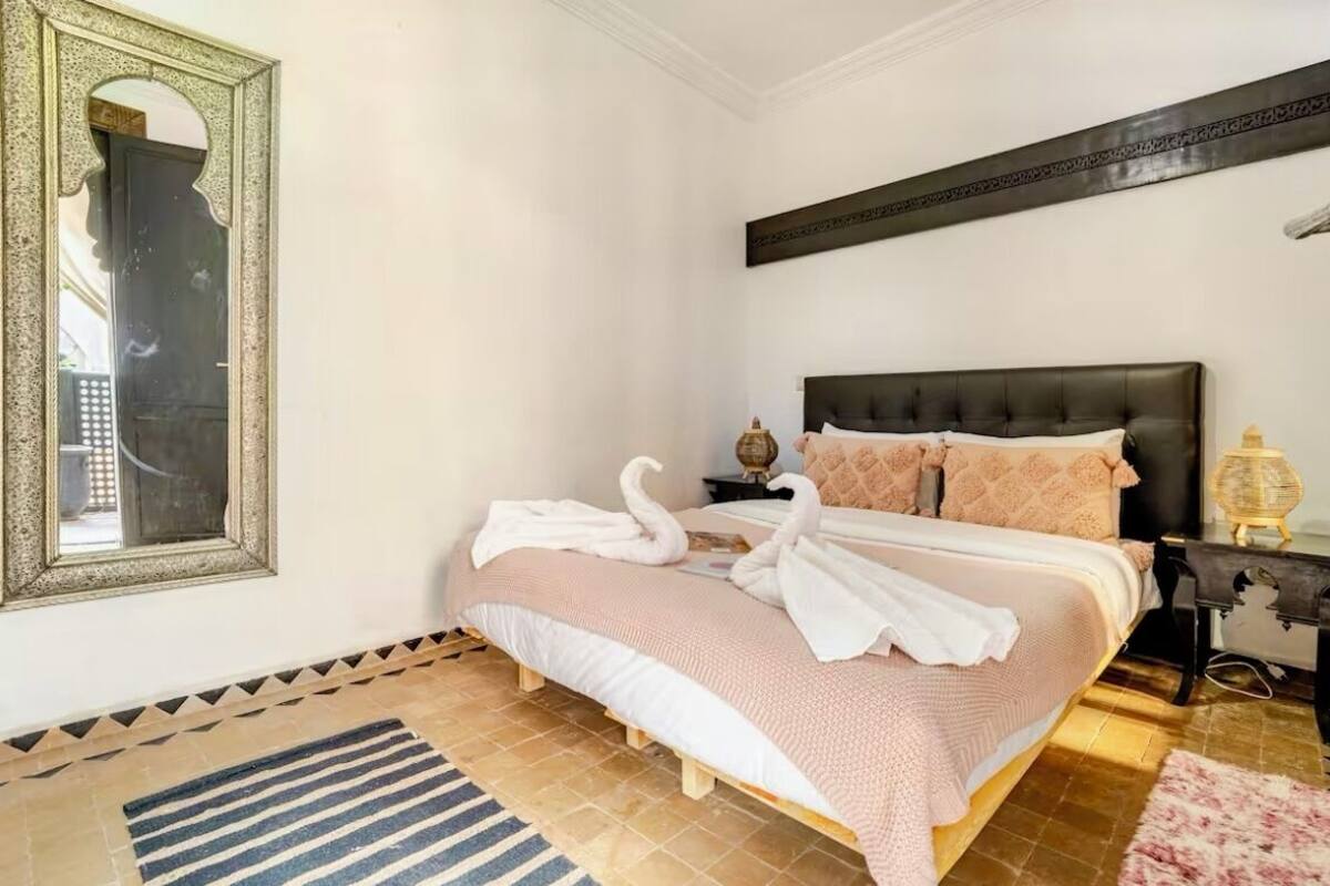 A bedroom with a bed, a mirror, a bedside table, and a lamp.