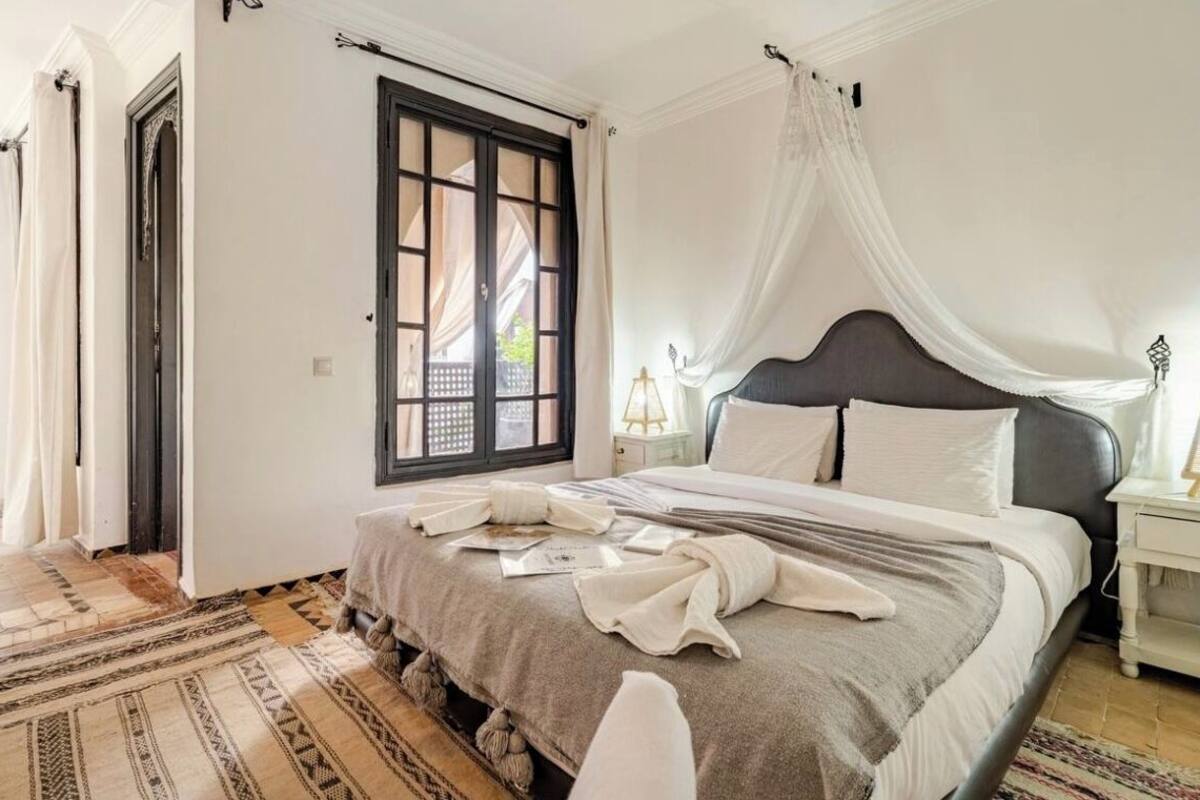 A bedroom with a bed, a nightstand, a window with curtains, and a patterned rug.