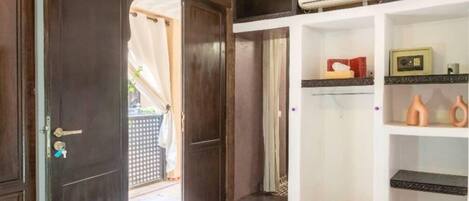 A room with a bed, a wardrobe, a shelf with decorative items, and a door leading to an outdoor area.