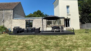 Une maison à deux étages dotée d’un patio aménagé avec du mobilier d’extérieur et un grand parasol.